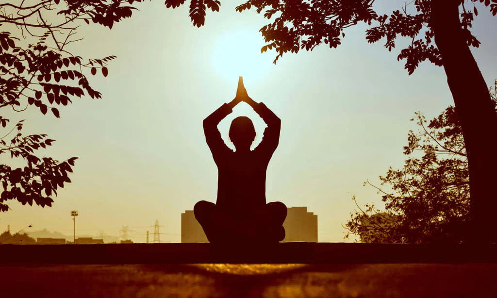 Persona meditando al atardecer en posición de loto, simbolizando bienestar y equilibrio natural que aportan los suplementos de Naturecan